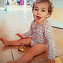 Emelia participe au concours pour gagner de l'argent avec cette photo : toddler, child, floor, toy, curly_hair, onesie, sitting, smiling, indoor, tile_floor, home_interior, play, furniture, rocking_chair, shelf, heart_overlay, happy, person, cute, young_child