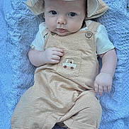 Carter is registered to the contest to win money with this photo: baby, infant, child, hat, overalls, beige_clothing, blanket, blue_blanket, texture, foot, hand, face, eyes, cute, portrait, outdoor, relaxing, sitting, soft_lighting, clothing