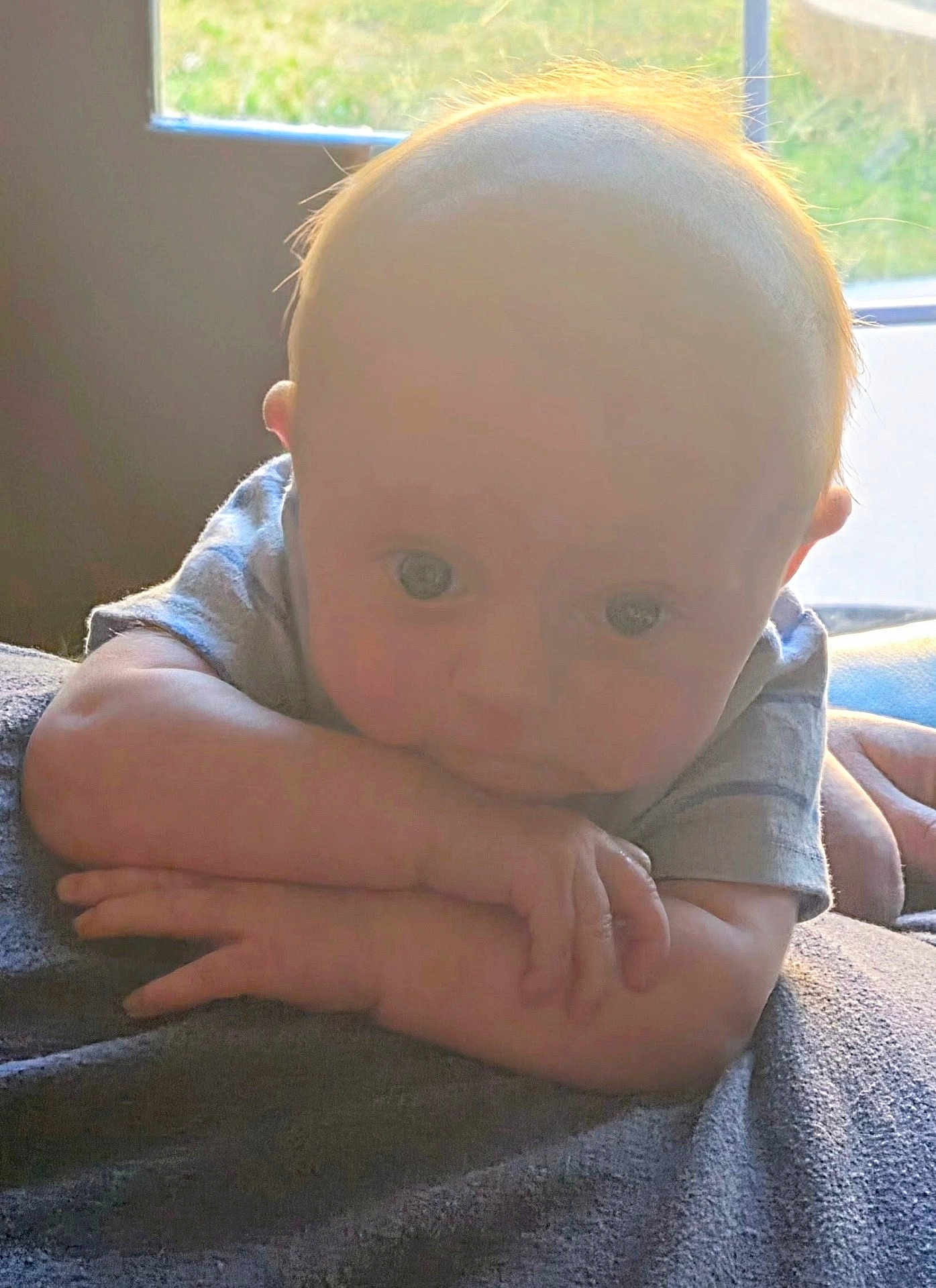 Garrison is registered to the contest to win money with this photo: baby, infant, tummy_time, arms, hands, window, sunlight, backlight, blanket, portrait, cute, skin, eyes, pajamas, gaze, indoor, soft_light, hair, forehead, newborn