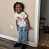 child, smiling, standing, indoor, tshirt, jeans, teddy_bear, wall, floor, doorway, bathroom, tile_floor, wood_floor, black_shoes, happy, person, casual_clothing, young_child, hair, home