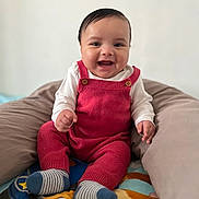 Timéo a rejoint le concours — aidez-le/la à gagner de superbes lots ! baby, smiling, red_overalls, white_shirt, cushion, blanket, striped_socks, indoor, child, happy, cute, portrait, seated, infant, knitwear, colorful, soft_furniture, playful, closeup, young_child