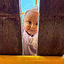 toddler, child, face, curious, playground, wood, yellow_bar, outdoor, blue_sky, smile, clothing, person, baby, cute, young_child, daylight, play, peek, portrait, fun