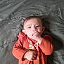 Sharon is registered to the contest to win money with this photo: baby, child, infant, orange_clothing, hand_in_mouth, blanket, lying_down, indoors, cute, young_child, face, portrait, person, sleepwear, soft_texture, small_hands, head, eyes, mouth, resting