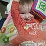 Sharon is registered to the contest to win money with this photo: baby, child, smiling, orange_clothing, tulle_skirt, soft_toy, alphabet_block, blanket, floral_pattern, cute, playful, infant, lying_down, indoors, person, happy, closeup, face, toddler, baby_girl
