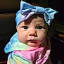baby, blanket, blue_bow, car_seat, child, colorful_clothing, cute, expression, face, headband, hoodie, indoors, infant, looking_at_camera, portrait, seated, soft_lighting, tie_dye, warm_colors, young_child