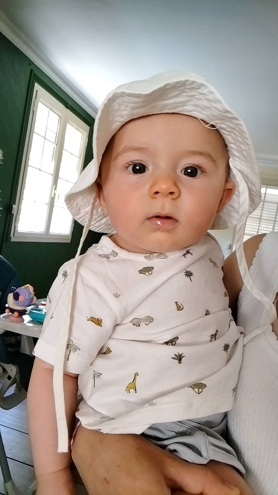 Nino participe au concours pour gagner de l'argent avec cette photo : animal_print, baby, big_eyes, child, curious, daylight, face, floor, furniture, hand, hat, holding, home, indoor, person, portrait, shirt, skin, white_hat, window