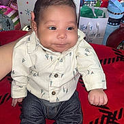 Romeo is registered to the contest to win money with this photo: baby, infant, child, clothing, shirt, jeans, socks, red_blanket, holiday_decorations, gift_bags, christmas, indoor, person, cute, smile, face, hand, seated, festive, portrait
