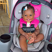 Journii is registered to the contest to win money with this photo: baby, child, smiling, car_seat, pink, gray, baby_holding_foot, hair_clip, cute, happy, indoor, floor_tiles, seatbelt, infant, toddler, person, small_child, dimples, playful, young_child