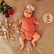 Ariana is registered to the contest to win money with this photo: baby, infant, flower_headband, coral_romper, plush_toy, elephant_toy, wooden_teether, red_roses, quilted_bedspread, birthday_badge, milestone, lying_down, cute, child, portrait, baby_boy, baby_girl, soft_lighting, indoor, celebration