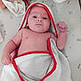 baby, baby_gesture, bare_chest, changing_mat, child, cute, fresh, indoor, infant, lying_down, newborn, patterned_mat, portrait, raised_fist, red_trim, resting, skin, small_hand, soft_towel, towel