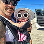 Chevelle joined the competition — help win amazing prizes! man, baby, sunglasses, hat, baby_carrier, outdoor, sunny, blue_sky, car, open_car_door, tattoo, mustache, smile, white_tank_top, child, person, holding, portrait, casual, daylight