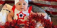 Chevelle joined the competition — help win amazing prizes! baby, infant, red_tinsel, festive_clothing, headband, star_pattern, blanket, sparkly_backdrop, celebration, cute, portrait, indoors, holiday_decor, smiling, chubby_cheeks, decorative, bright_colors, soft_texture, seated, adorable