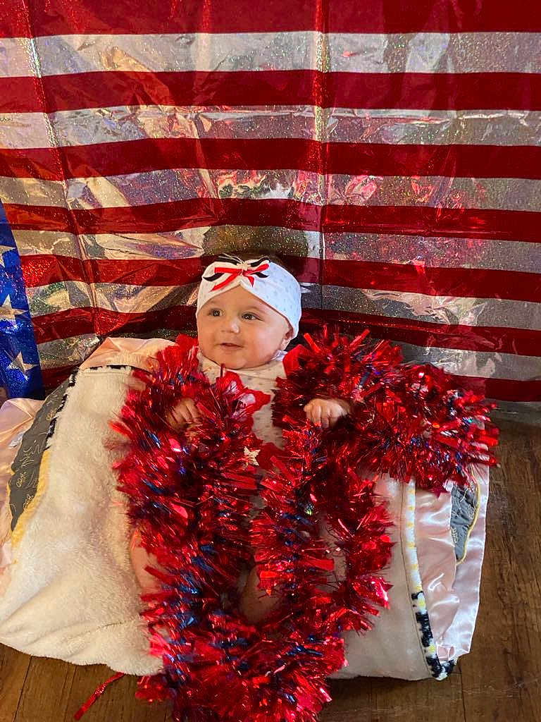 Chevelle joined the competition — help win amazing prizes! baby, tinsel, blanket, headband, red, blue, white, american_flag, patriotic, smiling, indoors, floor, festive, decorations, child, cute, holiday, soft, wrapped, sitting