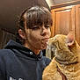 woman, cat, orange_tabby, indoor, kitchen, hoodie, pet, affection, licking, closeup, face, human, animal, feline, love, holding, casual, warm_lighting, portrait, domestic
