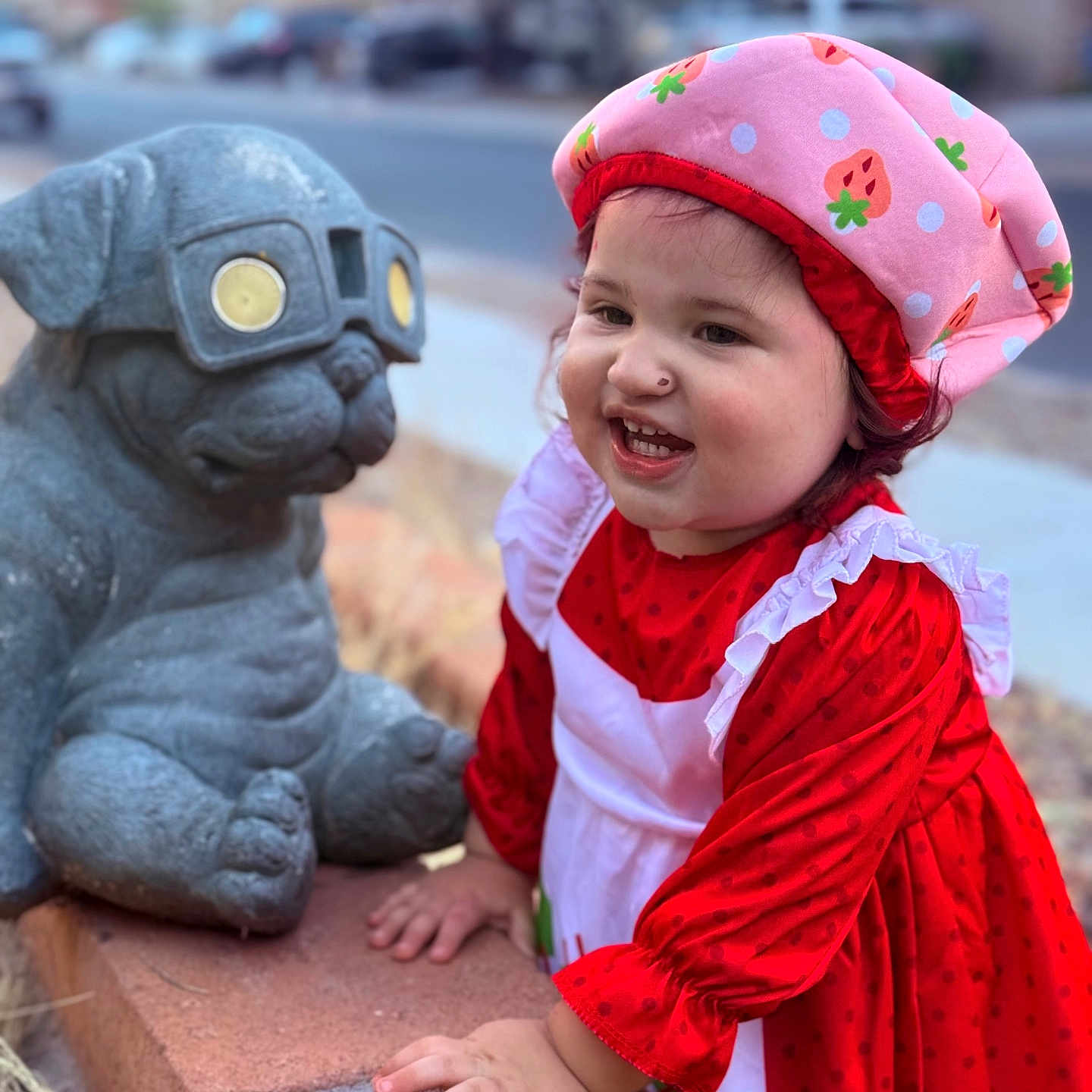 Elleanna joined the competition — help win amazing prizes! brick_ledge, child, cute, daylight, glasses, happy, outdoor, person, pink_hat, playful, portrait, pug_statue, red_dress, side_view, smiling, stone_statue, strawberry_pattern, suburban, toddler, young_child