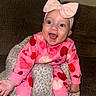 baby, bow, bright_eyes, child, couch, cozy, cute, floral_cushion, happy, headband, heart_pattern, home, indoors, infant, pink_clothing, portrait, seated, small_hands, smiling, socks
