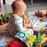 Ewen participe au concours pour gagner de l'argent avec cette photo : baby, child, toy, doll, brush, floor, blanket, colorful, indoor, play, plaything, toddler, red_hair, remote_control, stuffed_animal, patterned_blanket, clothing, sitting, curious, head