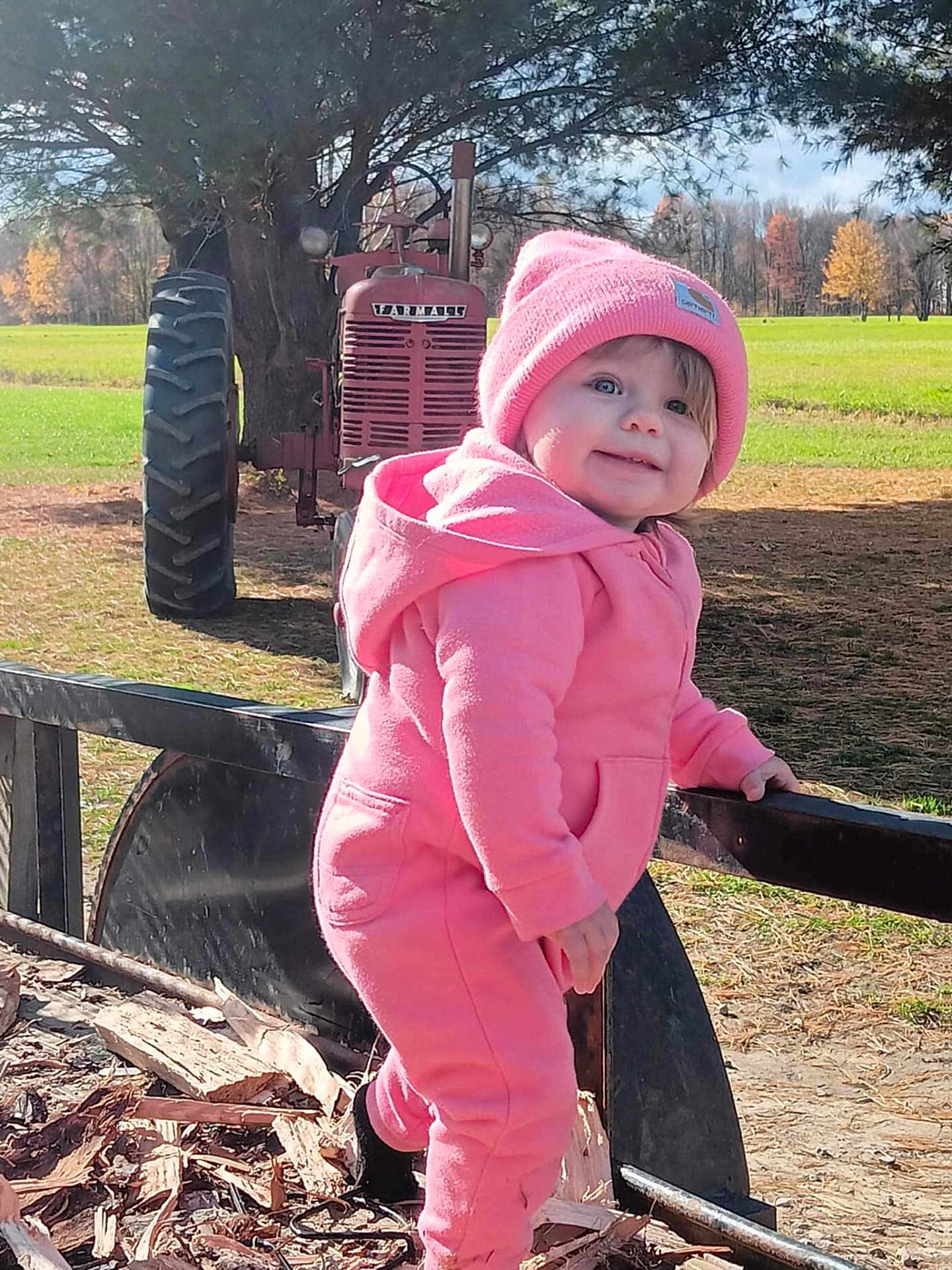 Gracie joined the competition — help win amazing prizes! baby, cap, clothing, coat, face, grass, hat, head, jacket, machine, nature, outdoors, pants, person, photography, plant, portrait, sitting, tire, wheel