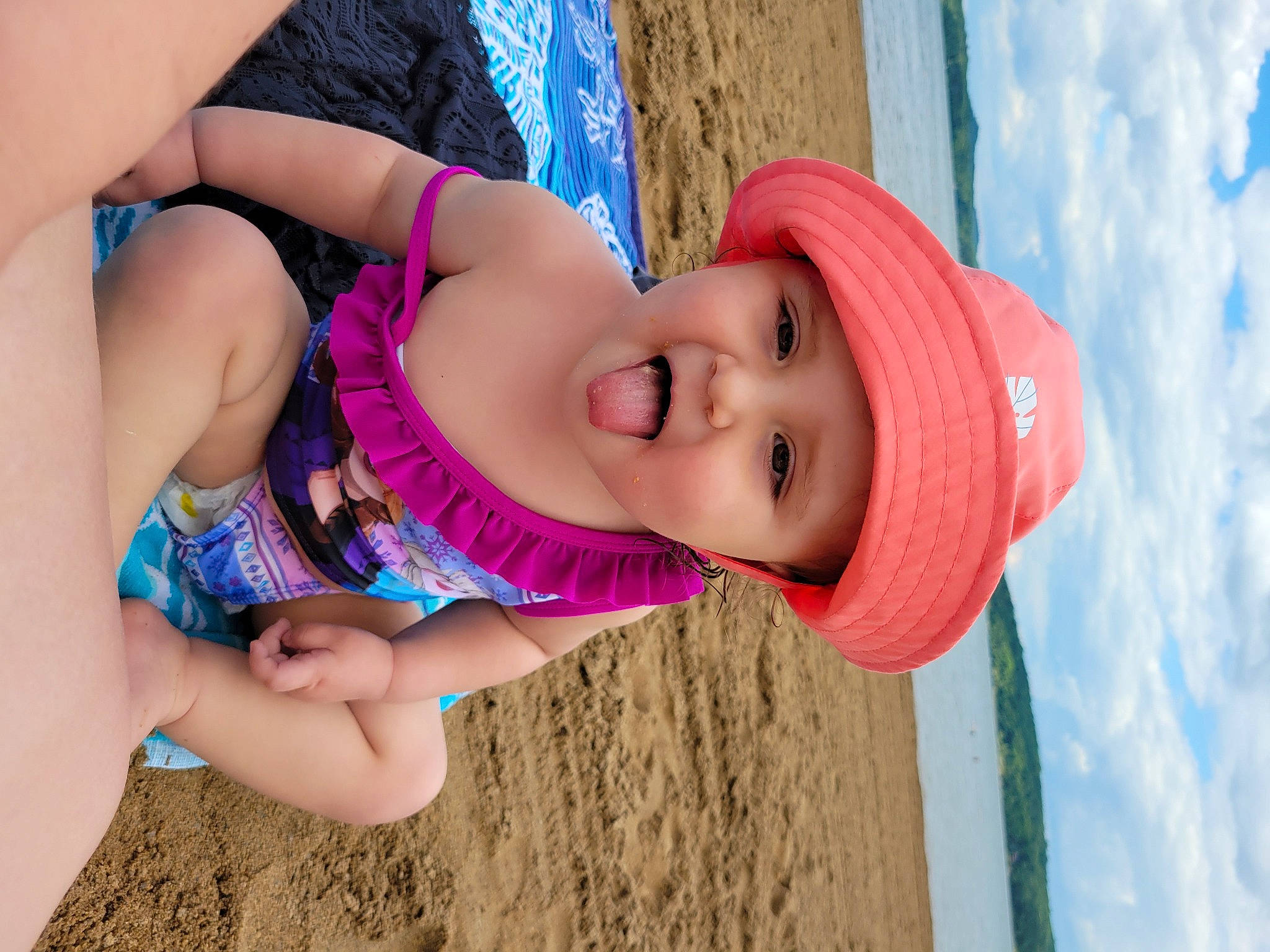 Amelia Rose is registered to the contest to win money with this photo: arm, azure, beach, blue, child, finger, fun, hand, happy, hat, headwear, human_body, leisure, people_in_nature, person, pink, skin, smile, sun_hat, toddler