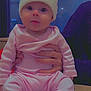 baby, child, infant, hat, knit_hat, pink_clothing, socks, hands, wooden_table, indoor, person, cute, seated, face, eyes, apparel, warm_clothing, holding, background_sign, portrait
