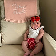 Macie is registered to the contest to win money with this photo: baby, child, smile, red_bow, headband, armchair, blanket, knitted_blanket, embroidery, red_and_white_clothing, plaid, infant, cute, happy, indoors, person, seated, cozy, furniture, portrait