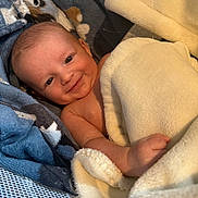 Kash Donoghue is registered to the contest to win money with this photo: baby, infant, newborn, smiling, blanket, towel, cozy, wrapped, lying_down, face, eyes, hand, head, cheek, bassinet, soft_texture, skin, portrait, cute, nestled