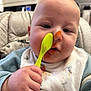 baby, child, spoon, messy_face, bib, high_chair, food, orange_food, hand, clothing, indoor, kitchen, person, face, cushion, feeding, closeup, cute, expression, toddler