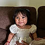 Lindsay Reyes is registered to the contest to win money with this photo: toddler, child, smile, white_dress, bow, couch, brown_furniture, hand, sitting, indoors, curly_hair, cute, happy, portrait, baby, person, clothing, bracelet, fabric, home