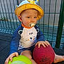 toddler, child, hat, pacifier, ball, green_ball, red_ball, sitting, outdoor, fence, clothing, shorts, long_sleeve_shirt, barefoot, play, toy, baby, young_child, person, daylight