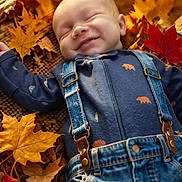 Koah is registered to the contest to win money with this photo: baby, smiling, fall, autumn_leaves, overalls, blue_clothing, outdoor, nature, child, cute, sleeping, seasonal, happy, portrait, infant, relaxing, colorful, leaf_litter, casual_clothing, peaceful