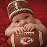 Koah joined the competition — help win amazing prizes! baby, infant, football, hat, red_blanket, sports, kc_chiefs, cute, child, portrait, closeup, hand, face, lying_down, knitted_hat, american_football, sports_fan, soft_texture, indoor, adorable