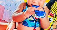 Milani joined the competition — help win amazing prizes! baby, child, smiling, curly_hair, hair_bows, blue_swimsuit, indoor, person, playing, sitting, lap, colorful_background, green_wall, yellow_wall, toy, hand, skin, face, cute, happy