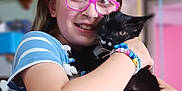 Rudy is registered to the contest to win money with this photo: girl, child, cat, black_cat, glasses, hugging, bracelet, indoor, striped_clothing, happy, smiling, portrait, cute, pet, young, colorful_background, home, close_up, affection, casual