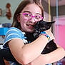girl, child, cat, black_cat, glasses, hugging, bracelet, indoor, striped_clothing, happy, smiling, portrait, cute, pet, young, colorful_background, home, close_up, affection, casual