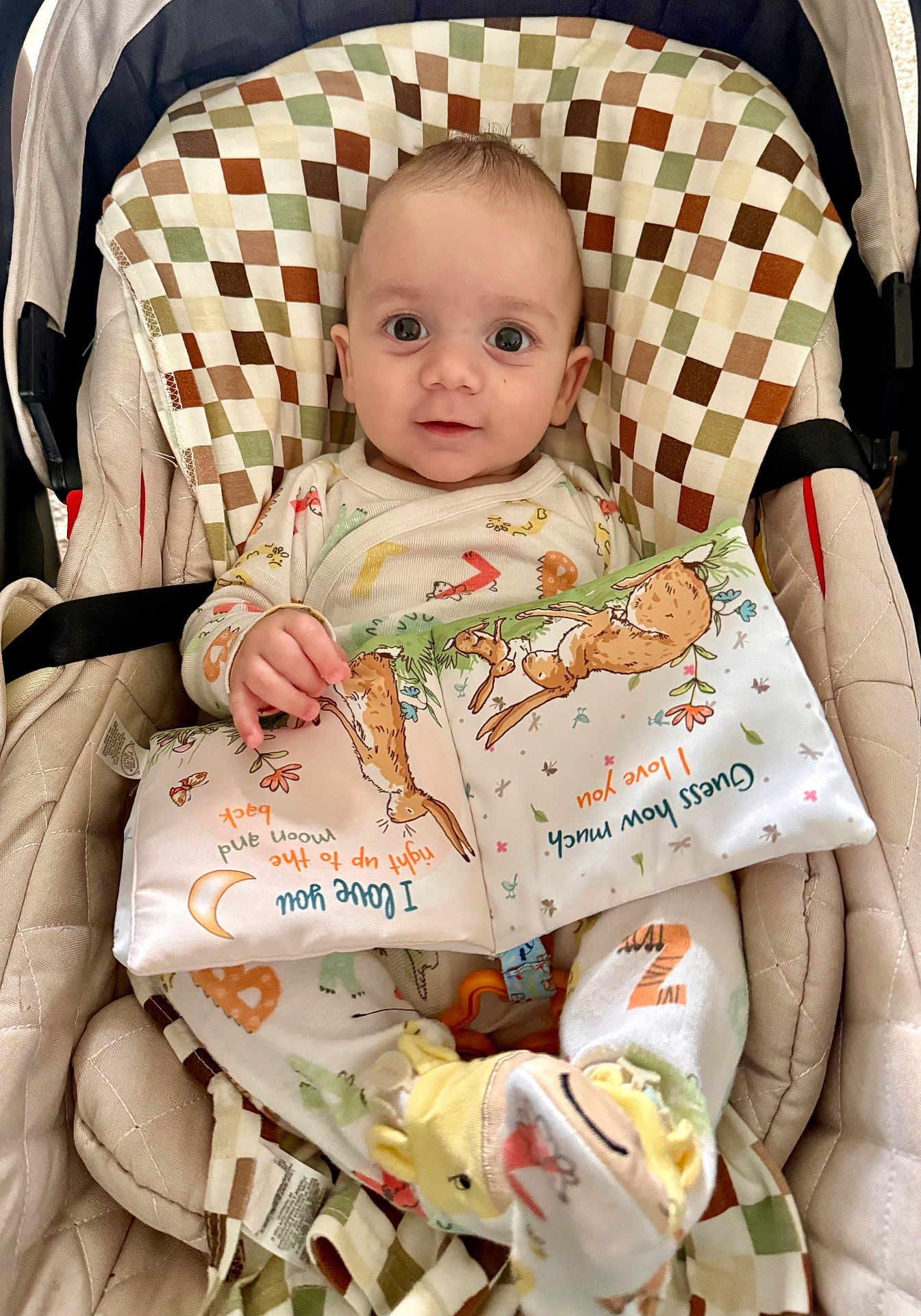Konstantin is registered to the contest to win money with this photo: baby, infant, seat, cushion, fabric_book, bunny, pajamas, slippers, animal_slippers, child, cute, indoors, smiling, face, hand, toy, soft_toy, patterned_fabric, colorful, closeup