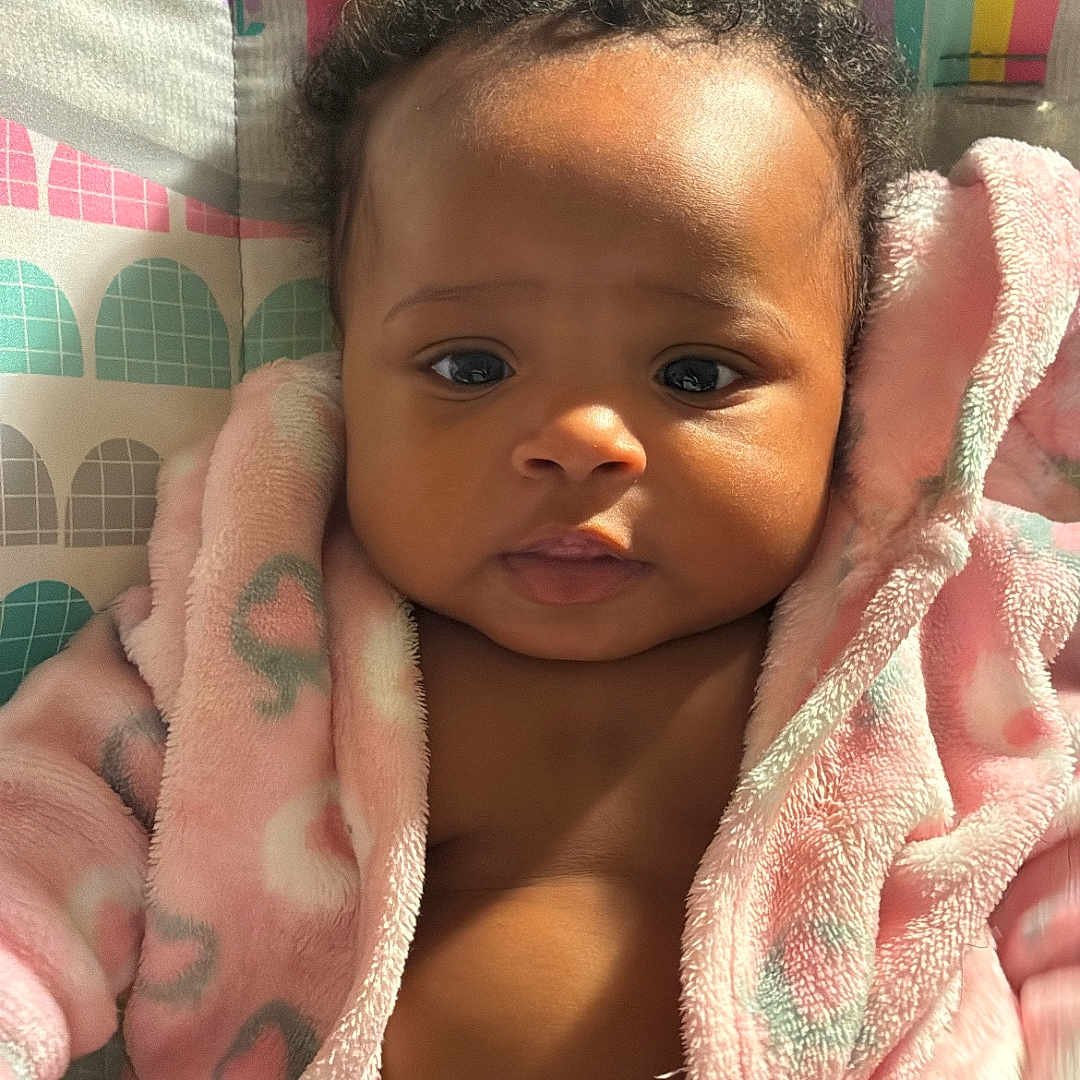 Blessyn joined the competition — help win amazing prizes! baby, infant, child, pink_robe, curly_hair, face, eyes, sunlight, indoor, colorful_background, rainbow, soft_texture, cute, portrait, young_child, warm_light, expression, skin, clothing, diaper
