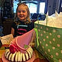 birthday, blonde_hair, cake, celebration, child, curtains, furniture, gift_bag, happy, home, icing, indoor, party, party_hat, person, polka_dots, present, smiling, table, young_girl