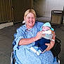 Bentley joined the competition — help win amazing prizes! woman, baby, wheelchair, hospital_gown, smiling, baby_clothes, sneakers, indoor, floor, hand, seated, person, holding, resting, headwear, medical_bracelet, background, light, expression, comfort