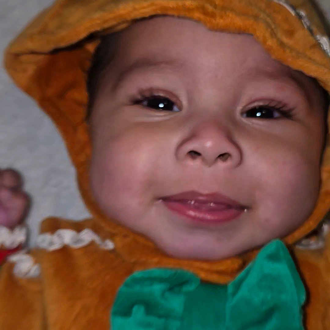 Gibo joined the competition — help win amazing prizes! baby, button, child, closeup, cute, eyelashes, face, green_bow_tie, happy, headwear, hooded_outfit, indoors, infant, orange_clothing, person, playful, portrait, smiling, soft_fabric, young_child