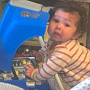 Gibo is registered to the contest to win money with this photo: baby, child, toy, blue_toy, striped_clothing, curious, indoor, hands, face, young_child, play, exploring, engine_toy, close_up, crawling, striped_onesie, plastic_toy, floor, background, person