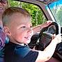 child, boy, steering_wheel, car_interior, adult_partial, sunglasses, window, trees, smiling, blue_eyes, blond_hair, hands, tattoo, dashboard, seat, portrait, daylight, road_trip, family, closeup
