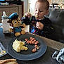 Cédric a rejoint le concours — aidez-le/la à gagner de superbes lots ! toddler, child, eating, plate, food, mashed_potatoes, sausages, table, toy, plush_toy, baby_bottle, kitchen, bread, fork, clothing, cupboard, chair, person, indoor, meal