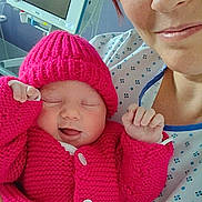 Claudia a rejoint le concours — aidez-le/la à gagner de superbes lots ! newborn, baby, adult, hospital, knitted_hat, knitted_sweater, pink_clothing, smile, sleeping, holding, person, medical_monitor, bedroom, closeup, human_face, comfort, parent, child, indoor, healthcare