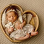 Paisley joined the competition — help win amazing prizes! baby, newborn, sleeping, heart_shaped_basket, lace_dress, knitted_toy, teddy_bear, blanket, headband, infant, cute, peaceful, soft_light, indoor, portrait, child, cozy, woven_basket, patterned_background, small_feet
