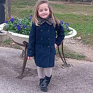 Mahé participe au concours pour gagner de l'argent avec cette photo : child, girl, coat, boots, flowers, planter, outdoor, park, path, grass, tree, building, sidewalk, smile, pose, cold_weather, fashion, nature, casual, confident