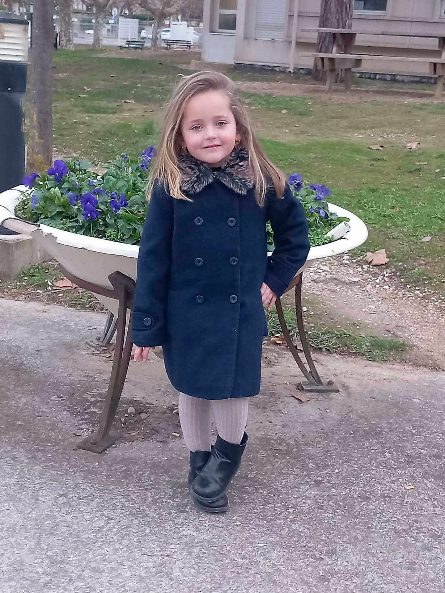 Mahé participe au concours pour gagner de l'argent avec cette photo : child, girl, coat, boots, flowers, planter, outdoor, park, path, grass, tree, building, sidewalk, smile, pose, cold_weather, fashion, nature, casual, confident