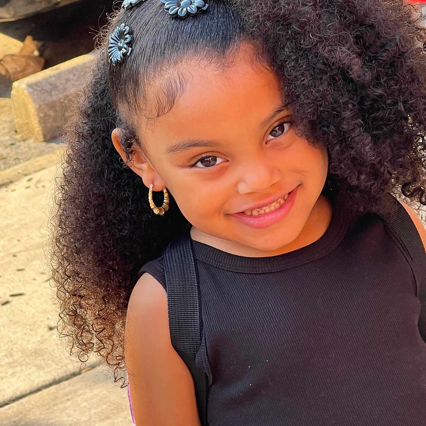 Penelope is registered to the contest to win money with this photo: accessories, black_top, child, closeup, confident, curly_hair, cute, earrings, face, fashion, girl, hair_accessories, happy, joyful, outdoor, person, portrait, smile, sunlight, young