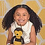 Penelope joined the competition — help win amazing prizes! accessories, bee_toy, bracelet, child, colorful, curly_hair, cute, earrings, girl, happy, indoors, person, plush_toy, portrait, sitting, smiling, studio, toy, white_dress, yellow_background
