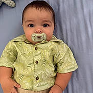 Samuel is registered to the contest to win money with this photo: baby, bed, blanket, child, clothing, cute, expression, eyes, face, hand, indoors, infant, knitted_toy, lying_down, pacifier, pants, portrait, shirt, soft_toy, young
