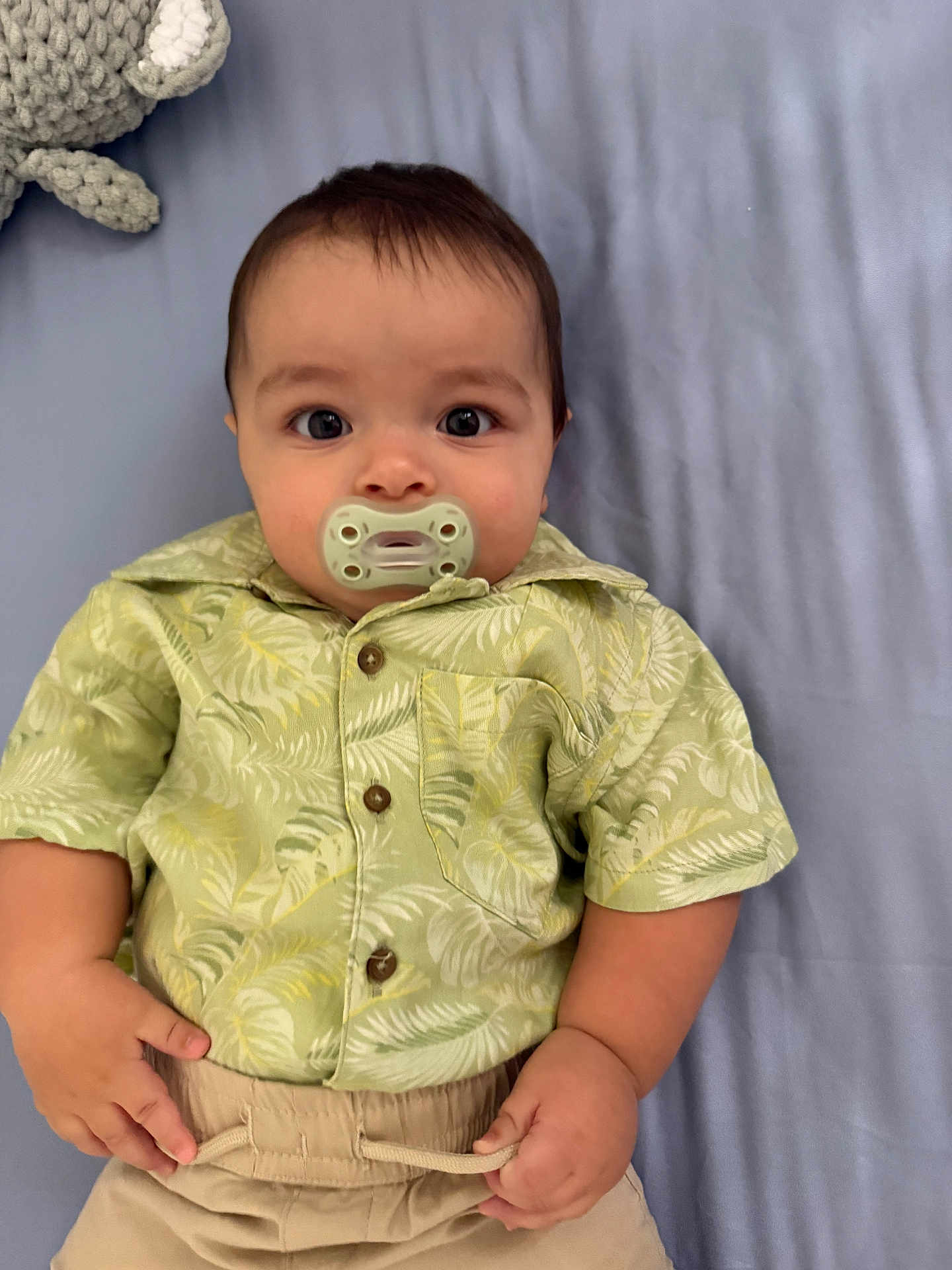 Samuel is registered to the contest to win money with this photo: baby, bed, blanket, child, clothing, cute, expression, eyes, face, hand, indoors, infant, knitted_toy, lying_down, pacifier, pants, portrait, shirt, soft_toy, young